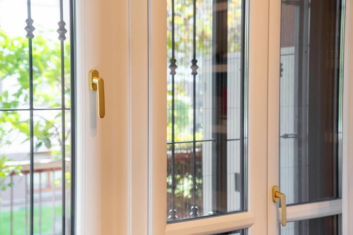 Daylight on white framed glazing with brass coloured lever handles and greenery outside.